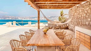 A wooden table with wicker chairs, a stone wall, and a view of the sea. - Villa 'The Blue Diamond' with Sea View, Wi-Fi and Air Conditioning (Mykonos)
