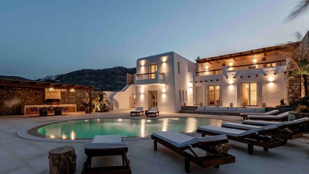 A modern villa with a swimming pool, lounge chairs, and a stone wall. - Villa 'The Blue Diamond' with Sea View, Wi-Fi and Air Conditioning (Mykonos)