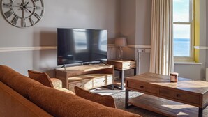 Ein Wohnzimmer mit Flachbildfernseher, Holzmöbeln, einer Uhr und einem Fenster mit Vorhängen.