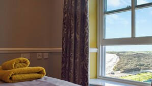 Ein Hotelzimmer mit Bett, einem Fenster mit Blick auf Strand und Grünflächen sowie einem gelben Handtuch auf dem Bett.