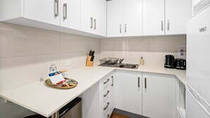 A modern kitchen with white cabinets, a stainless steel sink, and a coffee maker. - Clean Sunnybank Studio | AC | Near Shops | 4144D0 (Sunnybank)