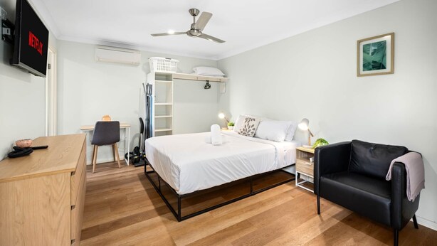 A modern hotel room with a bed, a desk, a chair, a black leather sofa, a ceiling fan, a TV, and a framed picture on the wall. - Clean Sunnybank Studio | AC | Near Shops | 4144D0 (Sunnybank)