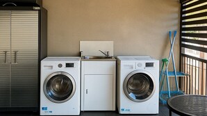 A laundry room with two front-loading washing machines, a small sink, and a cabinet. - Clean Sunnybank Studio | AC | Near Shops | 4144D0 (Sunnybank)