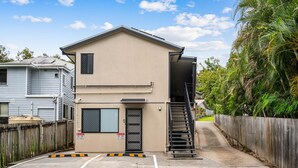 A two-story building with a beige exterior, a black door, and a visible staircase leading to the upper floor. - Clean Sunnybank Studio | AC | Near Shops | 4144D0 (Sunnybank)
