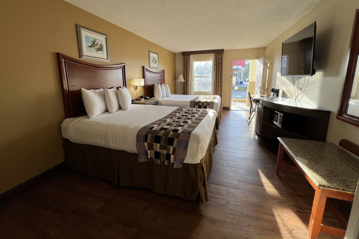 A hotel room with two beds, a desk, a TV, and a view of the outside.
