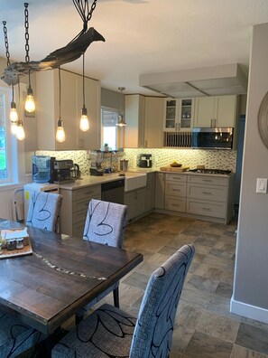 A modern kitchen with a central island, pendant lighting, and a dining area with a wooden table and chairs.