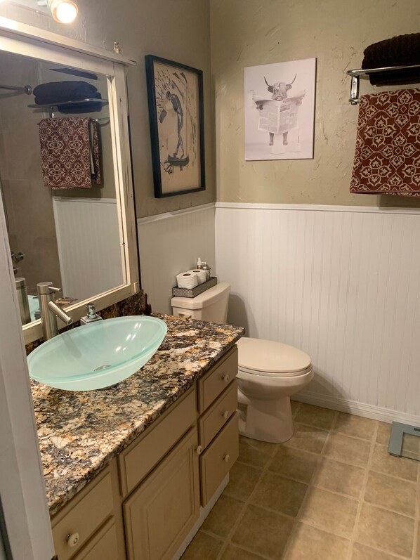 A bathroom with a glass sink, a toilet, and a mirror.