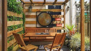 An outdoor patio with a wooden table and chairs, a decorative fan, and a wooden trellis with climbing plants.