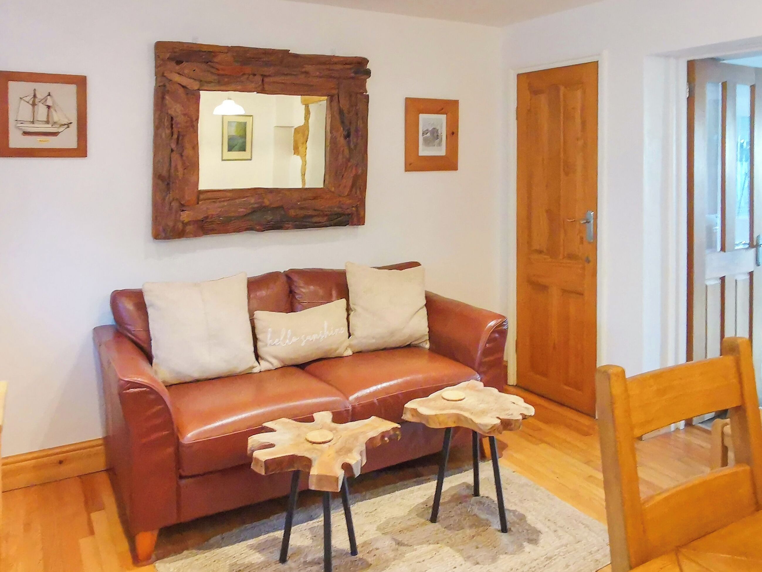 A brown leather sofa with two cushions, a wooden side table, a mirror, and framed pictures on the wall.
