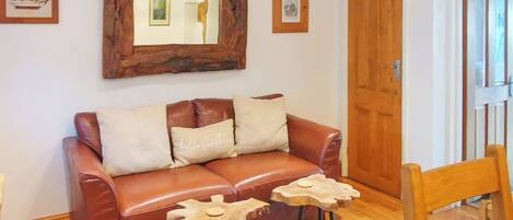 A brown leather sofa with two cushions, a wooden side table, a mirror, and framed pictures on the wall.