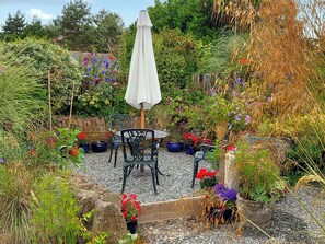 Un patio jardín con mesa y sillas, rodeado de macetas con plantas y un paraguas blanco.