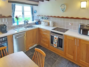 Una cocina con armarios de madera, lavavajillas, estufa, fregadero y ventana con cortinas.