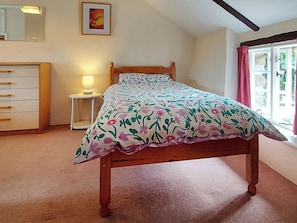 A bedroom with a wooden bed, a bedside table with a lamp, a dresser, a framed picture on the wall, and a window with curtains. - 2 bedroom accommodation in Chillaton, near Tavistock (Chillaton, near Tavistock)
