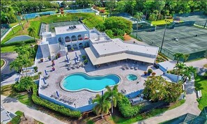 A hotel with a swimming pool, tennis courts, and a landscaped area with palm trees.