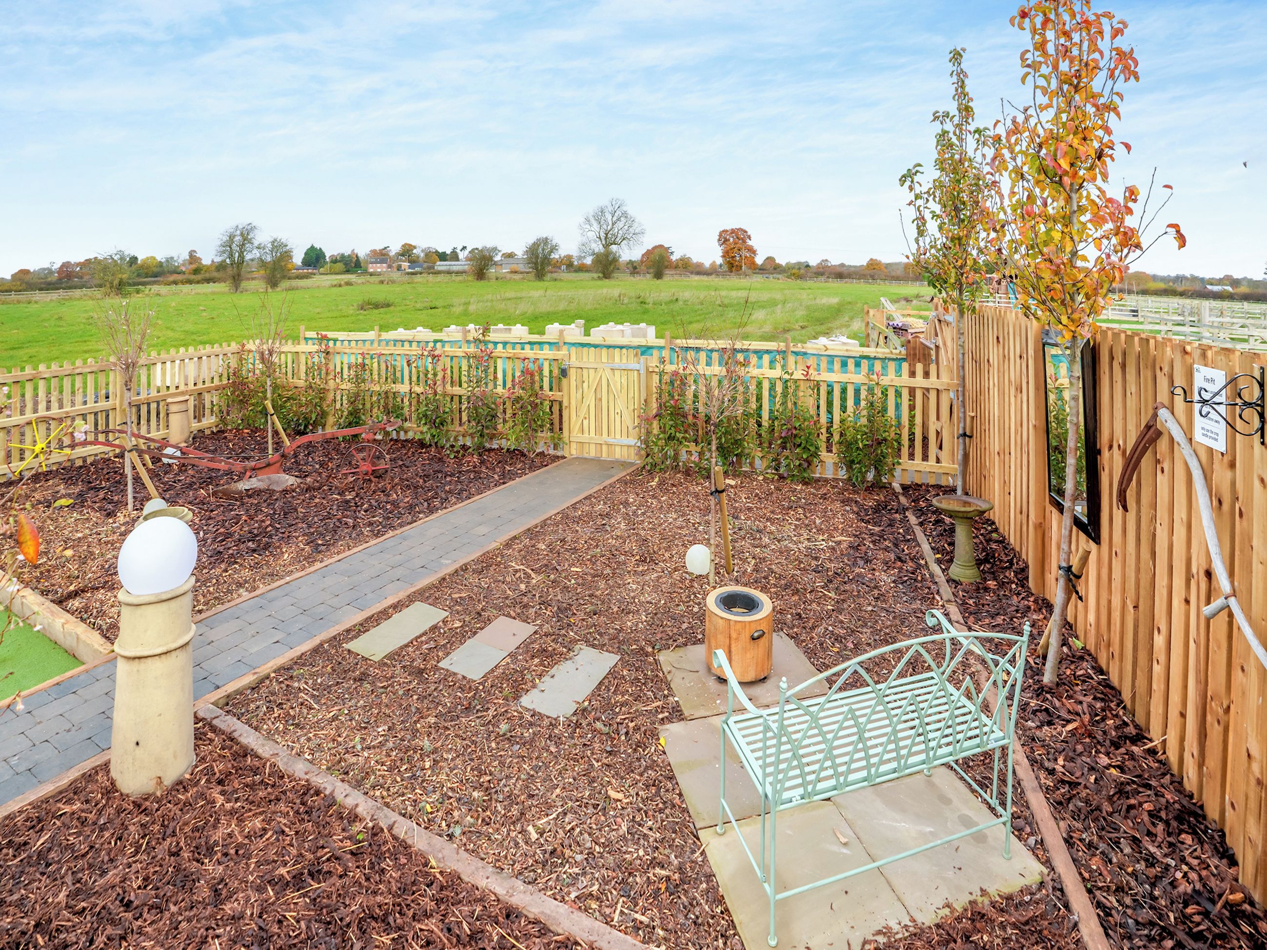 A garden with a wooden fence, a metal bench, and a pathway.