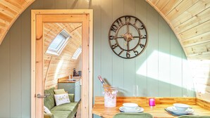 Una stanza accogliente con soffitto in legno, una sveglia a parete, un tavolo da pranzo con sedie e un letto che dà sul cucina.