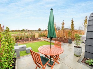A patio with a round table and chairs, a green umbrella, and a small lawn. - 1 bedroom accommodation in Church Broughton, near Derby (Church Broughton, near Derby)