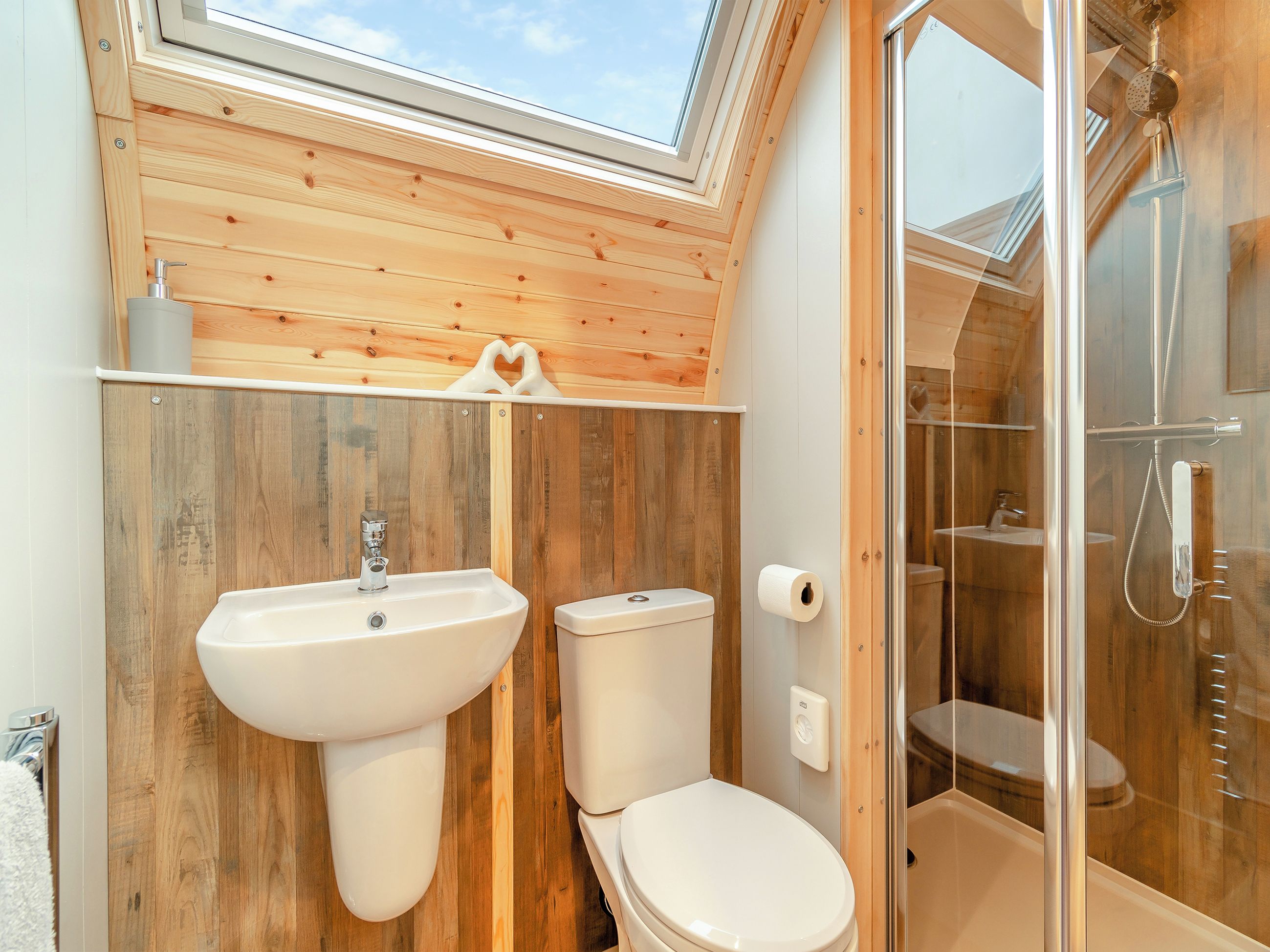 A bathroom with wooden walls, a skylight, a sink, a toilet, and a glass shower enclosure.