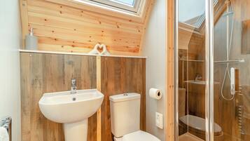 A bathroom with wooden walls, a skylight, a sink, a toilet, and a glass shower enclosure.