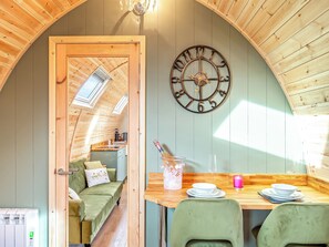 Une pièce chaleureuse avec un plafond en bois, une horloge murale, une table à manger avec des chaises et un lit donnant sur la cuisine.