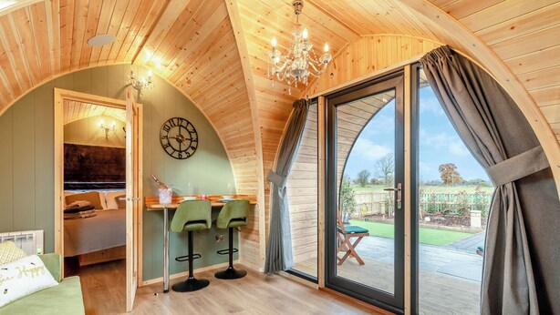 Una camera accogliente con soffitto in legno, un'area pranzo con due sedie, un letto e un'ampia finestra con tende.