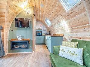 A cozy cabin interior with a fireplace, green sofa, and a kitchen area. - 1 bedroom accommodation in Church Broughton, near Derby (Church Broughton, near Derby)