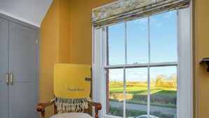 A room with a wooden chair, a yellow blanket, and a window with a view of a green landscape. - 2 bedroom accommodation in Burtle, near Glastonbury (Burtle, near Glastonbury)