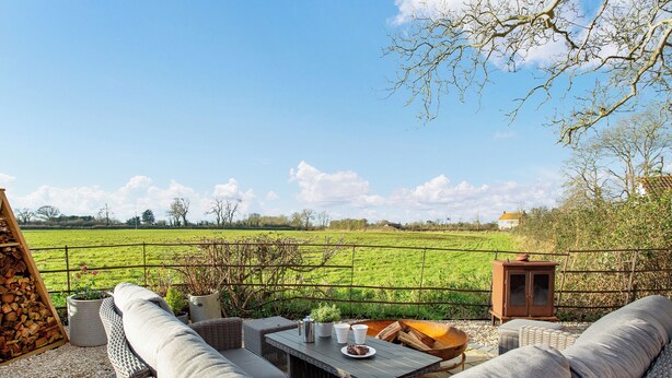 A patio with wicker furniture, a table with cups and a plate, and a view of a green field. - 2 bedroom accommodation in Burtle, near Glastonbury (Burtle, near Glastonbury)