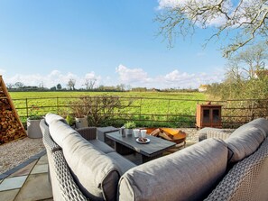 Un patio con muebles de mimbre, una mesa con tazas y un plato, y vistas a un campo verde.