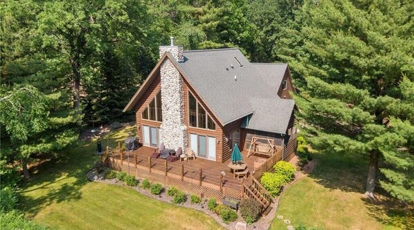 A log cabin with a stone chimney, wooden deck, and a fenced outdoor area. - Beautiful, modern log cabin on a great swimming and fishing lake with privacy! (Webster)