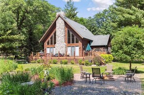A log cabin with a stone chimney, wooden deck, and outdoor seating area. - Beautiful, modern log cabin on a great swimming and fishing lake with privacy! (Webster)