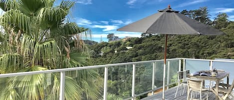 A wooden deck with a table and chairs, a large umbrella, and a view of a lush green landscape.
