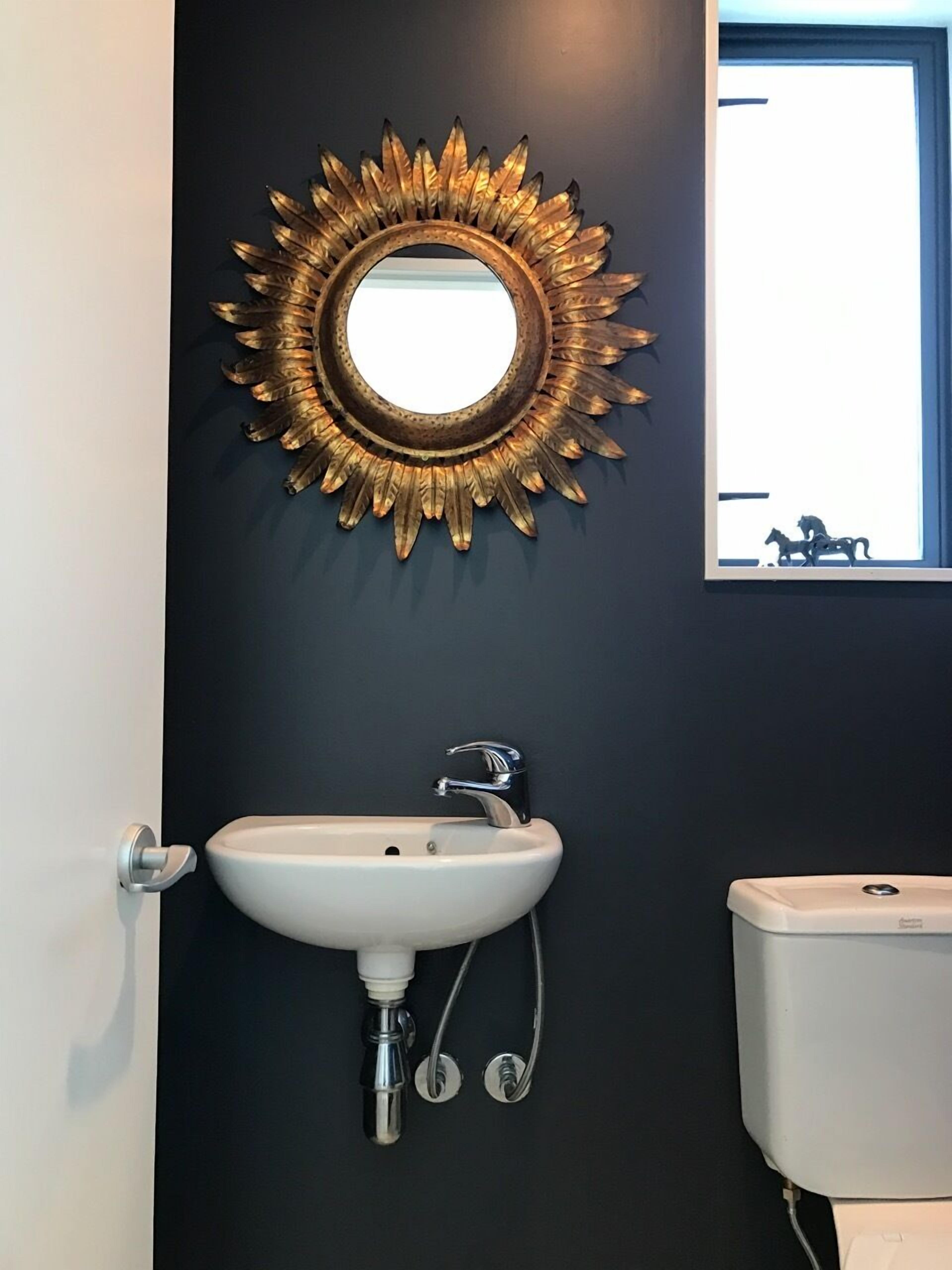 Un bagno con un lavandino bianco, uno specchio dorato e una finestra.