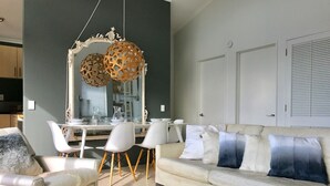 A modern living room with a white sofa, matching armchairs, and a dining area with a white table and chairs. - Villa Blanca in Palm Beach (Waiheke Island)
