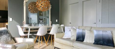 A modern living room with a white sofa, matching armchairs, and a dining area with a white table and chairs.
