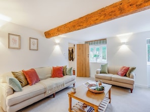 A living room with two sofas, a coffee table, and a wooden ceiling beam.