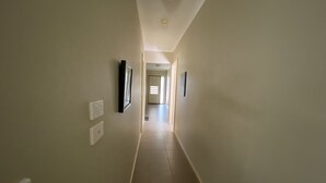 A narrow, well-lit hallway with light-colored walls and a tiled floor. There are wall-mounted light switches and a ceiling light fixture. - Whole House with 4 Queen Beds - Closer to Melbourne Airport - 8 Guests (Kurunjang)