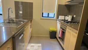 A compact kitchen with a stainless steel sink, a window, a trash bin, and a stove. - Whole House with 4 Queen Beds - Closer to Melbourne Airport - 8 Guests (Kurunjang)