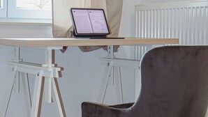 A room with a desk, a laptop, a chair, a window with curtains, and a radiator.