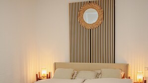 A neatly made bed with two rolled towels, a wall-mounted mirror, and two bedside lamps.