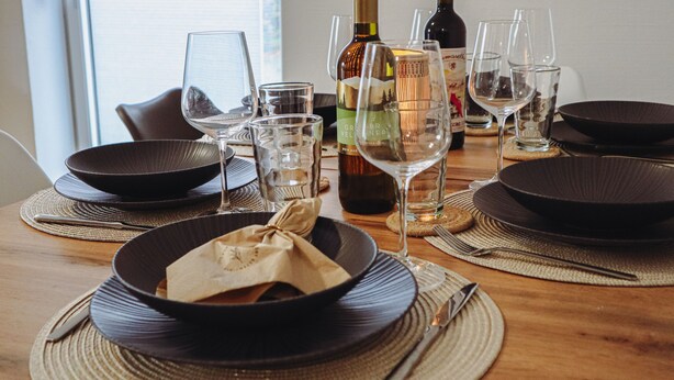 A dining table set with black plates, clear glasses, and a bottle of wine.