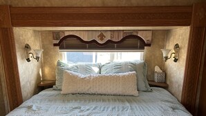 A neatly made bed with a quilted cover, two pillows, and a bedside table with a tissue box.