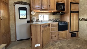 A compact kitchen with wooden cabinets, a stove, a microwave, and a refrigerator.