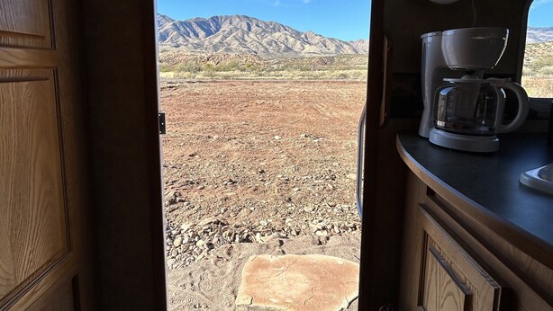 A kitchen with a coffee maker, a fire extinguisher, and a view of a desert landscape through an open door.