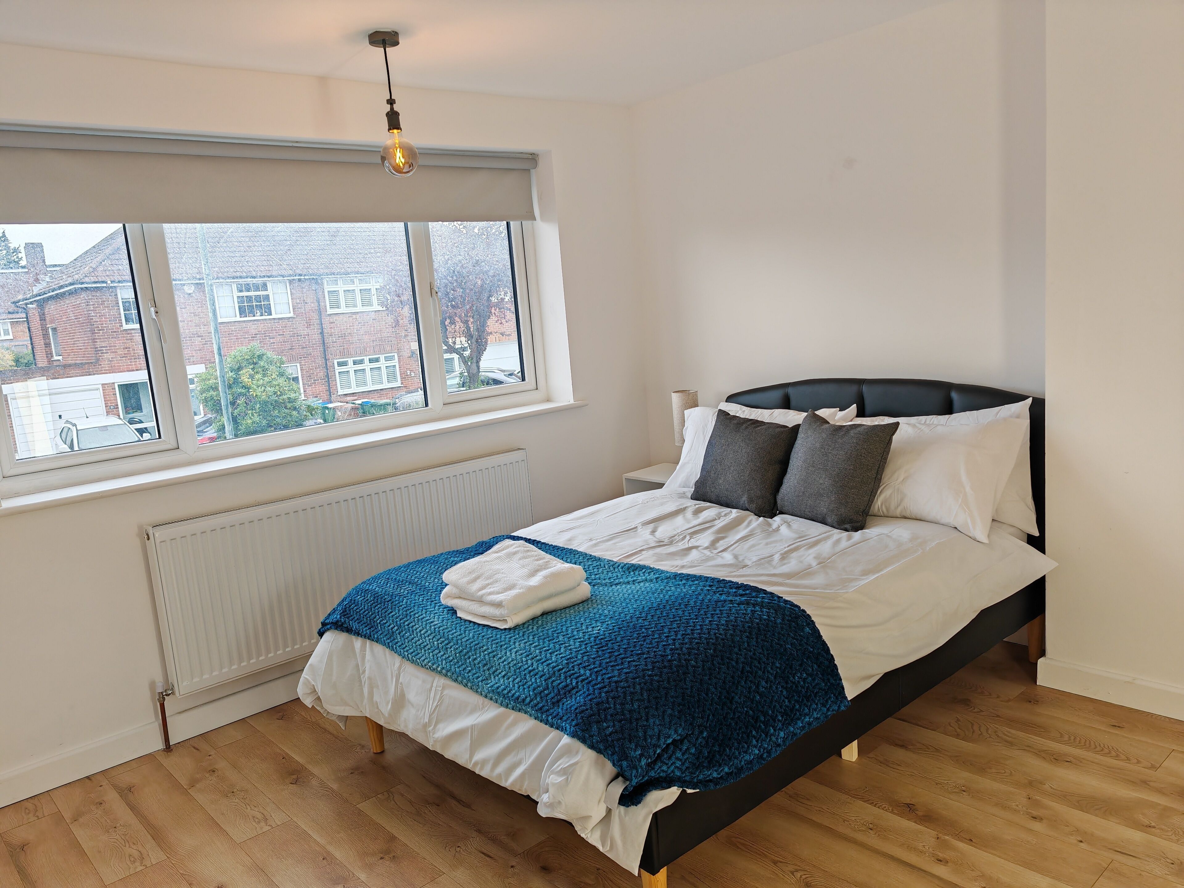 A bedroom with a bed, a window, a radiator, and a view of buildings outside.