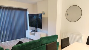 A modern living room with a green sofa, a flat-screen TV on a white stand, and a dining table with chairs. - Charming 5 Bedroom House in Bexley (Bexley)
