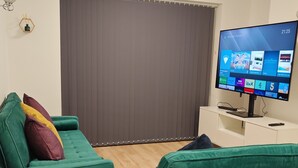 A modern living room with a green sofa, a small table, and a television displaying a streaming service interface. - Charming 5 Bedroom House in Bexley (Bexley)