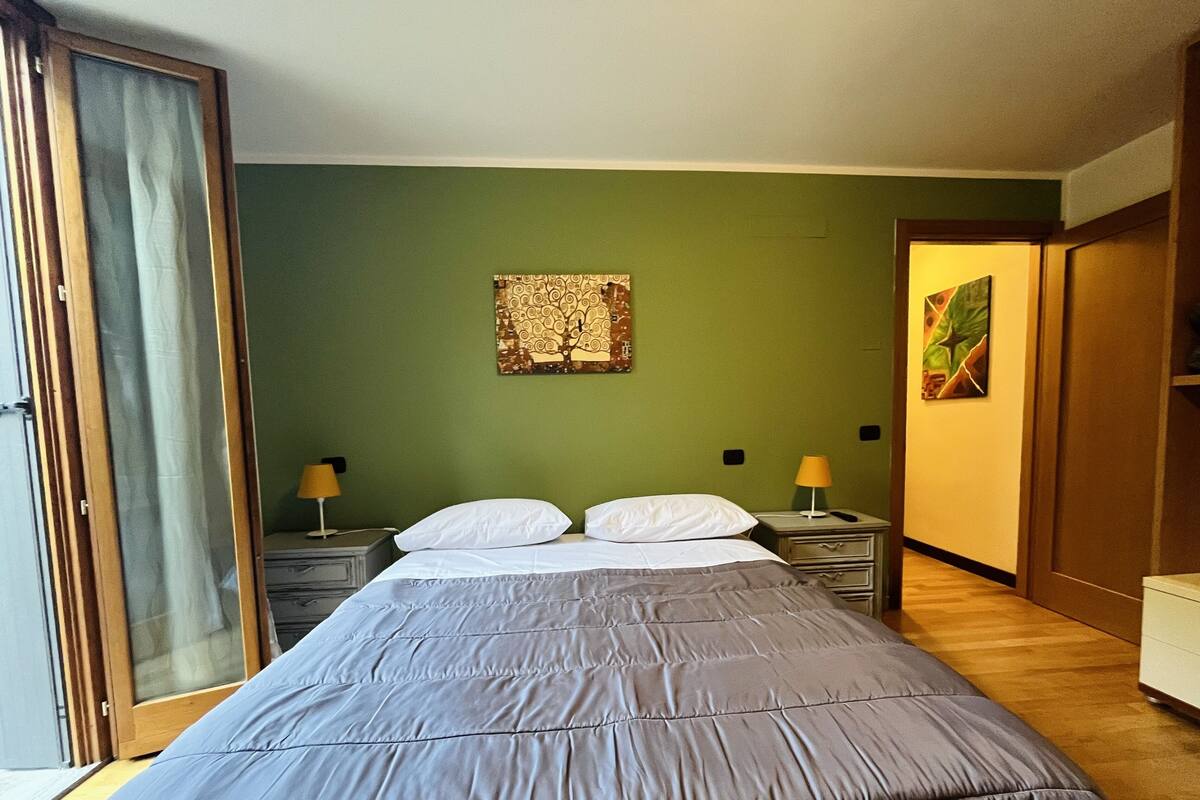 A bedroom with a bed, two bedside tables, a green wall, and a door.
