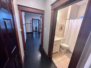 Un couloir menant à une salle de bain équipée de toilettes, d’un lavabo et d’un rideau de douche.