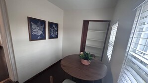 Un pequeño comedor con una mesa redonda, dos sillas, una planta en maceta y dos cuadros en la pared.